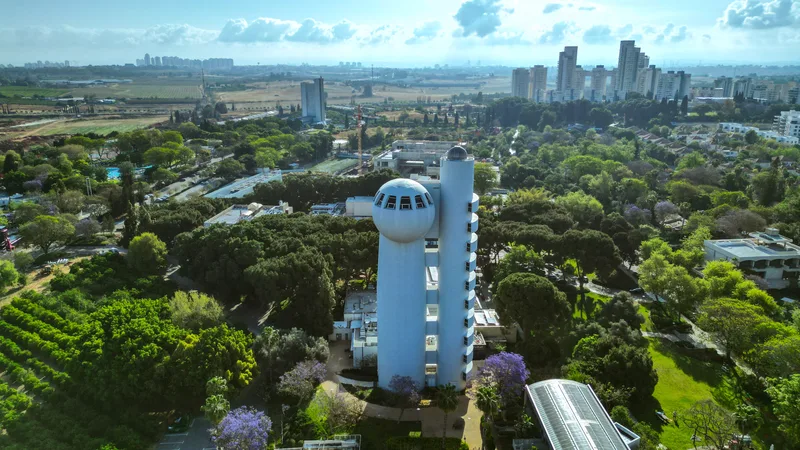 The Weizmann Institute campus in Rehovot from the air, the Koffler accelerator tower at its centre, jacarandas in bloom around it.